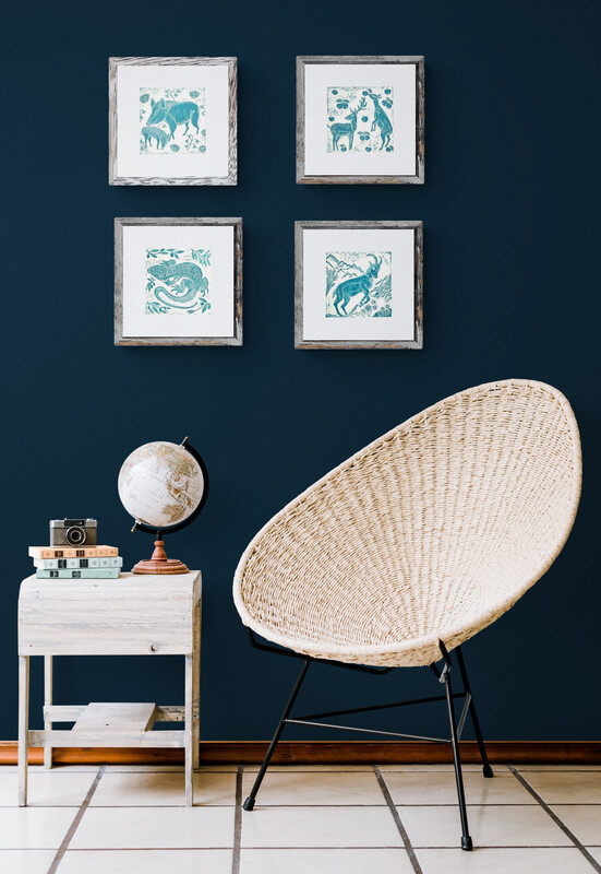 four framed small teal linoprints on a dark blue wall next to a contmporary pink basket chair